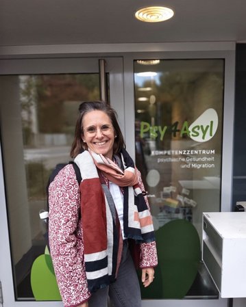 A woman with glasses and a scarf stands in front of the entrance to the Psychiatry and Migration Center 'Psy 4 Asylum.