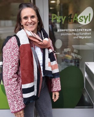 A woman with glasses and a scarf stands in front of the entrance to the Psychiatry and Migration Center 'Psy 4 Asylum.