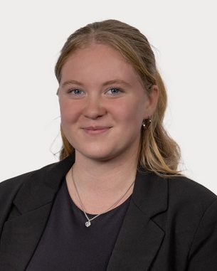 Young woman with blonde hair smiling in a black blazer. The background is neutral and bright.