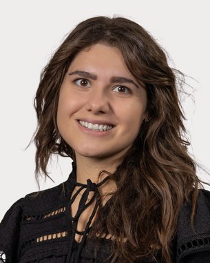 A smiling woman with long, curly hair is wearing a black top with decorative details.