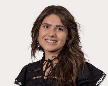 A smiling woman with long, curly hair is wearing a black top with decorative details.