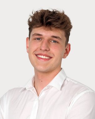 Young man with curly hair, smiling in a white shirt with his arms crossed. Neutral background.