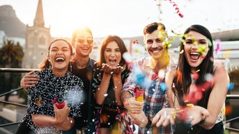 Five people are gathered together celebrating as they throw confetti into the air. The group is smiling and posing happily.