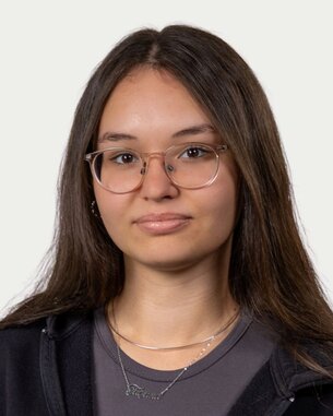 Young woman with long, straight hair and glasses, wearing a black hoodie and a gray blouse. She is looking directly at the camera.