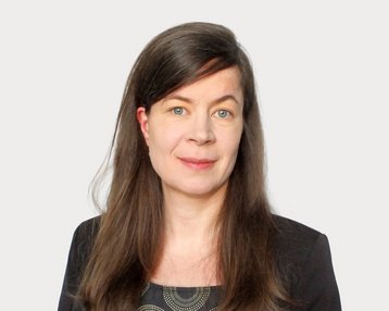 A woman with long brown hair and blue eyes is wearing a black top with a graphic pattern.