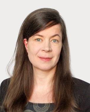 A woman with long brown hair and blue eyes is wearing a black top with a graphic pattern.