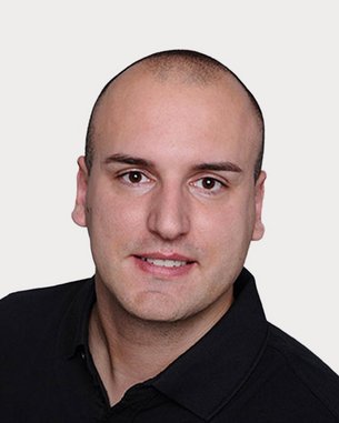 A man with short, smooth hair is wearing a black polo shirt and looking directly at the camera. The background is neutral.
