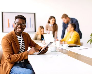 Young African American business man working with his tablet in front of his coworkers at boardroom