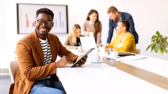 Young African American business man working with his tablet in front of his coworkers at boardroom