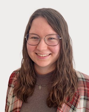 A smiling person with long, curly hair is wearing a checkered jacket and glasses. The background is neutral.