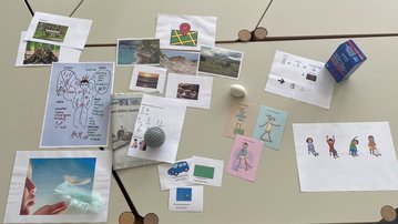 A collection of pictures and drawings on a table, including landscapes, illustrations, and a box of drinks.