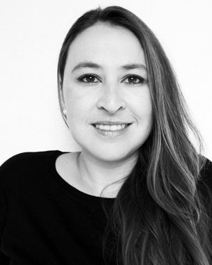 Eine Frau mit langen, braunen Haaren und einem freundlichen Lächeln trägt ein schwarzes Oberteil. Der Hintergrund ist neutral und hell.