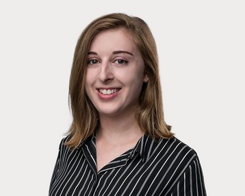 A young woman with long, curly hair is wearing a striped shirt and smiling at the camera. The background is neutral.
