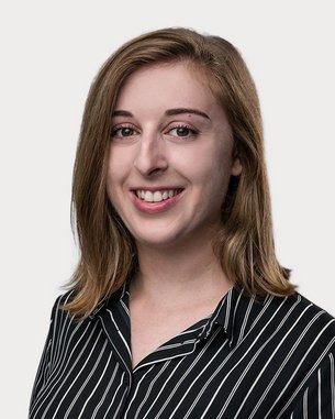 A young woman with long, curly hair is wearing a striped shirt and smiling at the camera. The background is neutral.