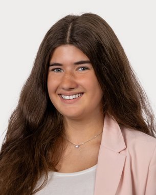 Young woman with long, curly hair, smiling in a light blazer and a white top. Neutral background.