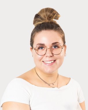 Young woman with a bun and glasses, wearing a white top, smiling warmly against a neutral background.