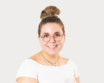 Young woman with a bun and glasses, wearing a white top, smiling warmly against a neutral background.