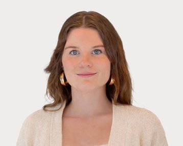Young woman with long brown hair and large earrings, wearing a light sweater and looking directly at the camera.